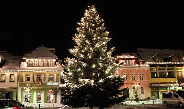 Ein geschmückter und beleuchteter Weihnachtsbaum vor einer beleuchteten Häuserzeile