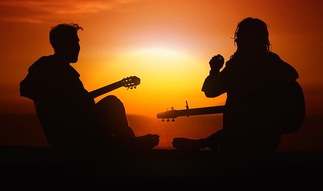 Silhouette von Jugendlichen mit Gitarren vor einem Sonnenuntergang. Symbolbild für den Text, der erklärt, warum Jugendliche abends oft lange wach und morgens müde sind.