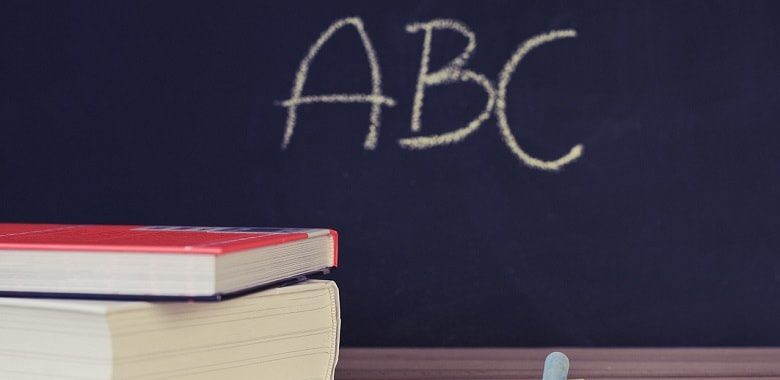 Eine Tafel mit den Buchstaben ABC. Davor Ein Stapel Bücher und bunte Kreide. Symbolbild für die häufigsten Wörter in deutschen Texten.