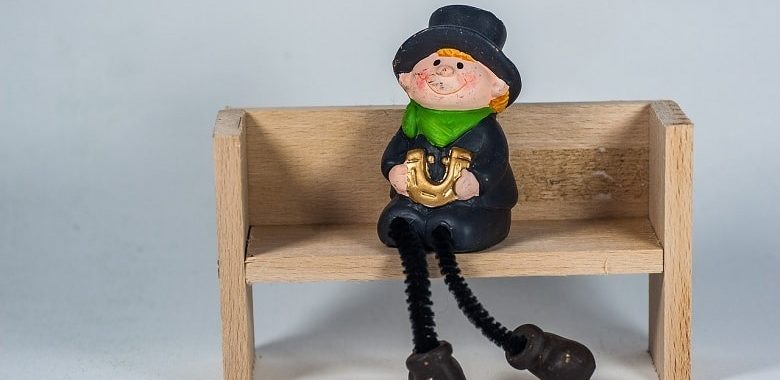 Eine Schornsteinfeger-Figur sitzt auf einer Bank und hält ein Hufeisen in der Hand. Symbolbild für die Erklärung des Sprichworts "Schornsteinfeger bringen Glück".