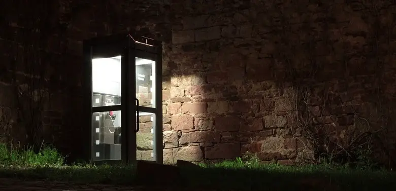 Eine alte Telefonzelle leuchtet in der Nacht. Symbolbild für die 100-Wörter-Geschichte "In der alten Telefonzelle", in der jemand wartet.