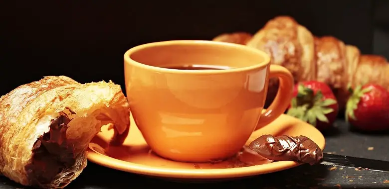 Eine Tasse Kaffee, ein Croissant und etwas Haselnussaufstrich. Symbolbild für den Beitrag zur Blogparade #Sonntagsglück.