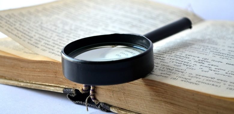Eine Lupe liegt auf einem alten, dicken geöffneten Buch. Symbolbild für den Text, der erklärt, warum die Seite nicht 100 Worte heißt und den Unterschied zwischen den Pluralformen für "Wort", "Worte" und "Wörter", erläutert.
