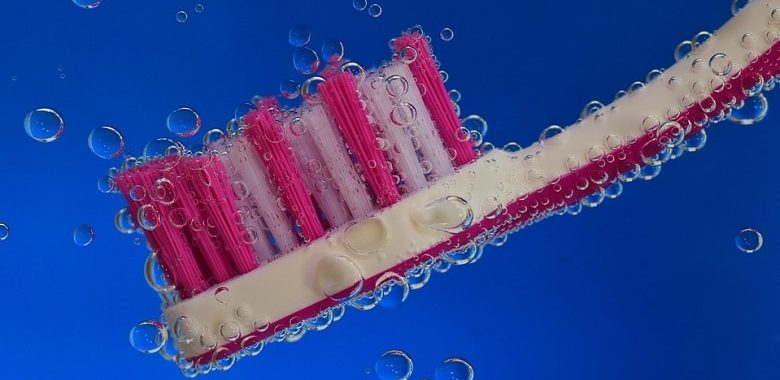 Eine Handzahnbürste unter Wasser, von der sich Luftblasen lösen. Symbolbild für den Text "Was ist besser: Handzahnbürste oder elektrische Zahnbürste?"