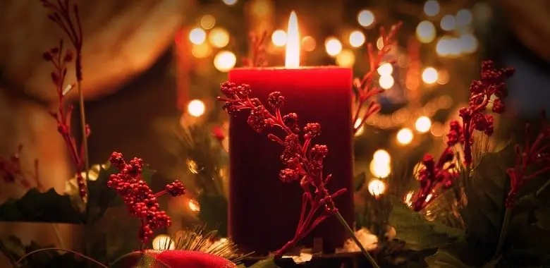 Eine angezündetet rote Kerze mit Weihnachtsschmuck. Symbolbild für schöne Geschichten im Advent.
