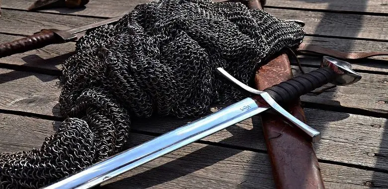 Ein Schwert liegt auf einem Kettenhemd. Symbolbild für Erklärung und Herkunft der Redewendung "Das Heft in die Hand nehmen".