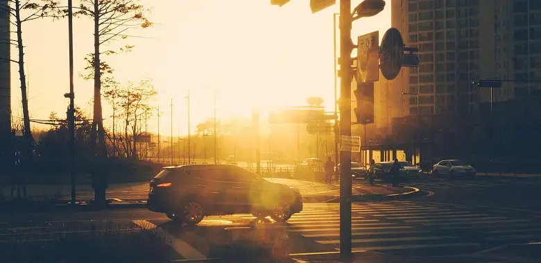 Eine Auto steht an einer Kreuzung. Das Sonnenlicht macht die Sicht schwierig. Symbolbild für 100 Wörter über Realität.