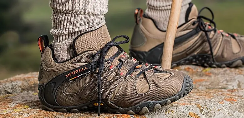 Zwei Füße in Wanderschuhen, dazwischen ein Wanderstock. Symbolbild für die Erklärung der Redensart "Etwas aus den Füßen haben".