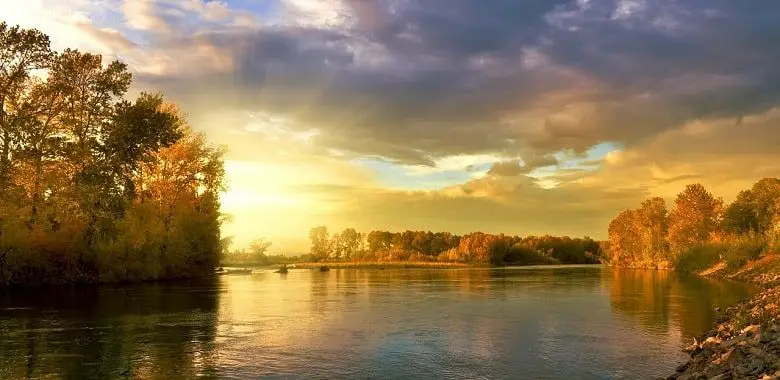 Ein See mit spätsommerlichen Bäumen im goldenen Sonnenuntergang. Symbolbild für den Monat September und die Herkunft und Erklärung seines Namens.
