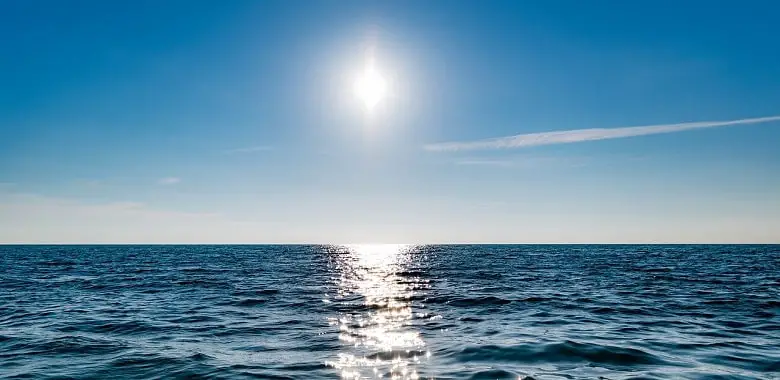 Die helle Sonne strahlt an einem blauen Himmel über dem Meer. Symbolbild für die Erklärung, warum manche Menschen niesen, wenn sie in die Sonne gucken.