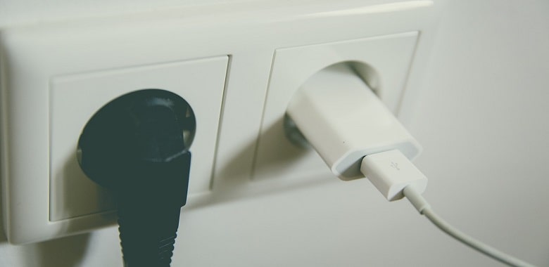 Ein Stecker und ein Ladegerät in einer Steckdose. Symbolbild für die Erklärung, ob es gefährlich ist, eine Ladegerät in einer Steckdose zu lassen.