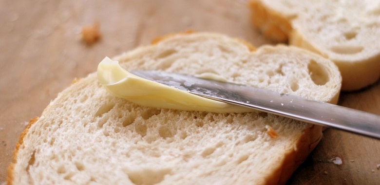 Mit einem Messer schmiert jemand Margarine auf ein Brot. Symbolbild für die interessante Geschichte zur Erfindung der Margarine.