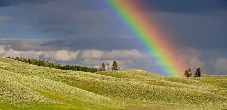 Ein Regenbogen berührt eine grüne Hügellandschaft. Symbolbild für die 100WÖRTER-Schülergeschichte "Mein größter Traum".
