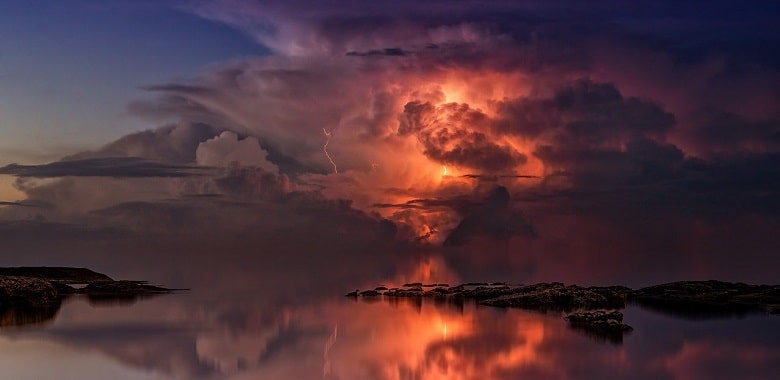 Ein leuchtendes Gewitter mit großen Wolken über einem See. Symbolbild für die 100WÖRTER-Schülergeschichte "Das Wetter von Malibu".