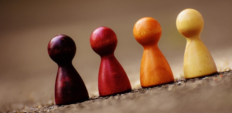 Vier Spielfiguren stehen auf einer Schräge. Symbolbild für die Erklärung der Redensart „ein schräger Typ sein“.