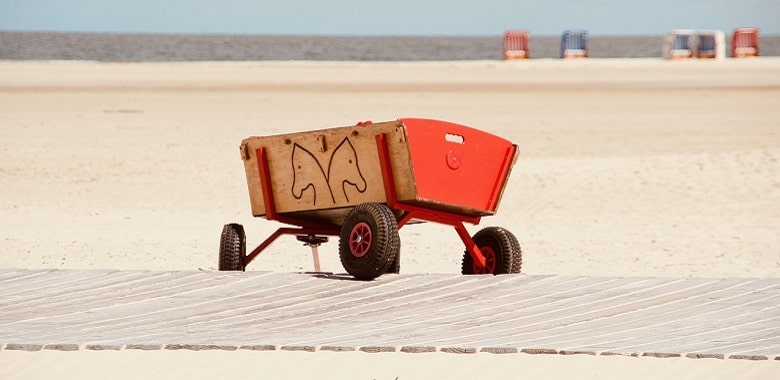 Ein Bollerwagen auf einem Bohlenweg am Strand. Symbolbild für die Erklärung des Brauchs, dass Männer am Vatertag herumziehen.