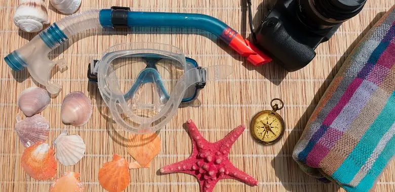 Taucherbrille, Schnorchel und Muscheln auf einer Decke. Symbolbild für die Erklärung, warum Spucke vor dem Beschlagen der Taucherbrille schützt.