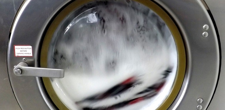 Nahaufnahme einer laufenden Waschmaschine. Symbolbild für die Erklärung der verschiedenen Waschmitteltypen Pulver, flüssig, Gel.